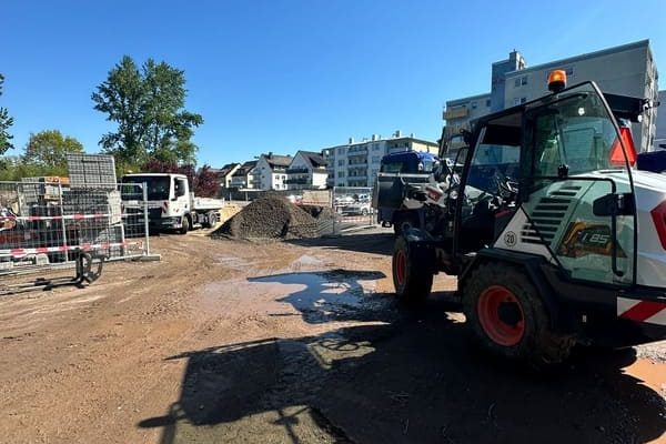 Baustelle mit Bagger, Lkw und Erdhaufen unter blauem Himmel.