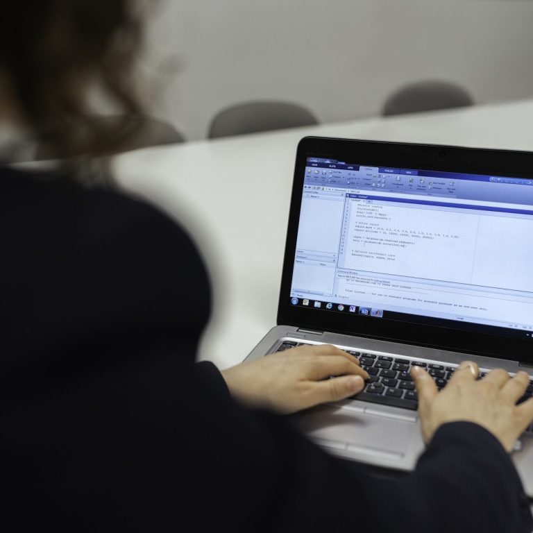 Jemand tippt auf einer Laptop-Tastatur, Code wird auf dem Bildschirm angezeigt.