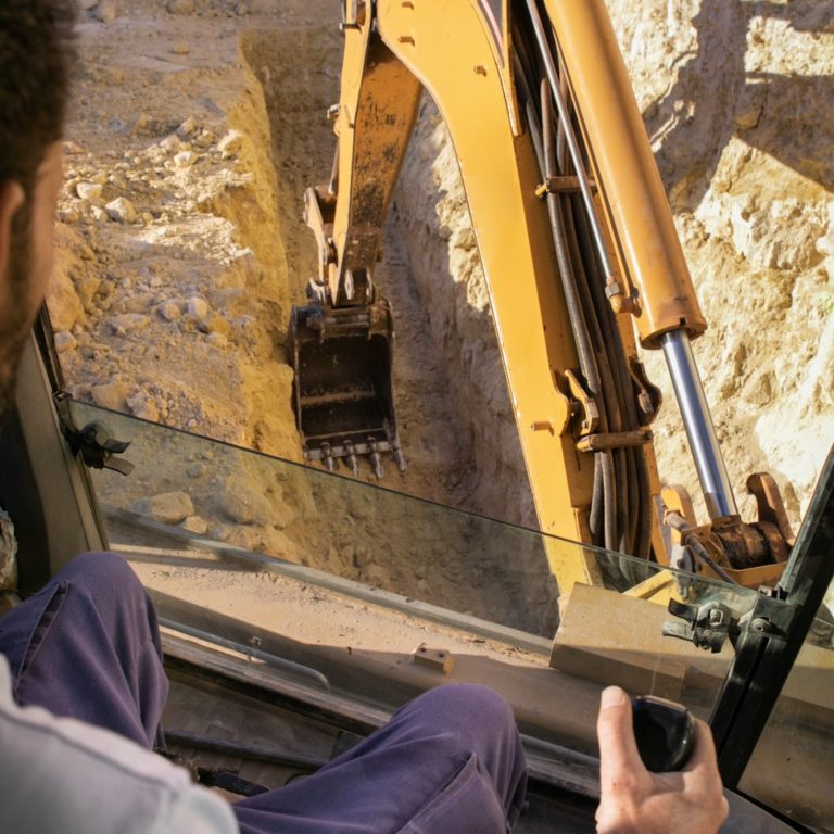 Blick aus einem Bagger auf eine Grube, Steuerung in der Hand des Fahrers.